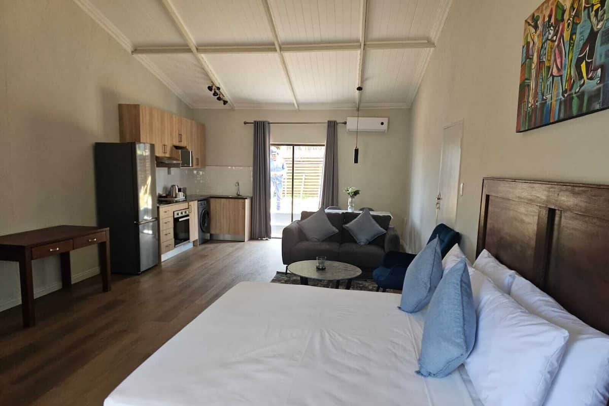 Een slaapkamer met een groot bed, een slaapbank, een klein tafeltje en een kitchenette op de achtergrond.