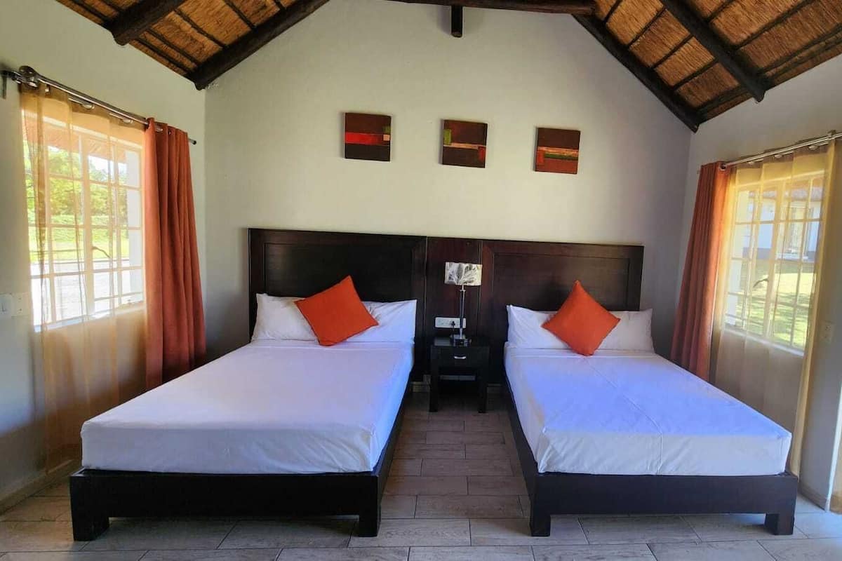 Een kamer met twee bedden, een houten plafond en een nachtkastje daartussen.