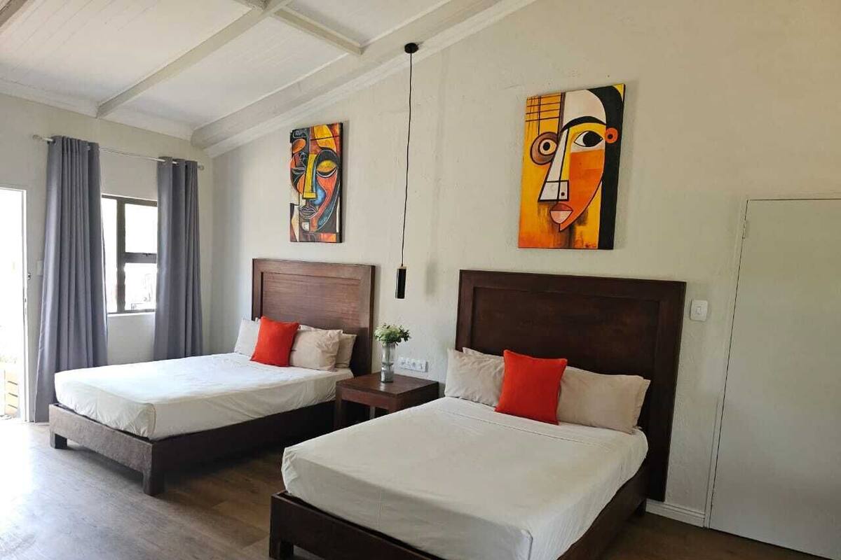 Een hotelkamer met twee bedden, houten hoofdborden en abstracte kunst aan de muren.