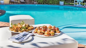 A poolside dining area with plates of appetizers and a white cushioned bench. - Shumba Valley Lodge Lanseria Airport (Lanseria)