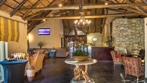 A spacious lobby with a high ceiling, stone walls, and a central wooden table. - Shumba Valley Lodge Lanseria Airport (Lanseria)