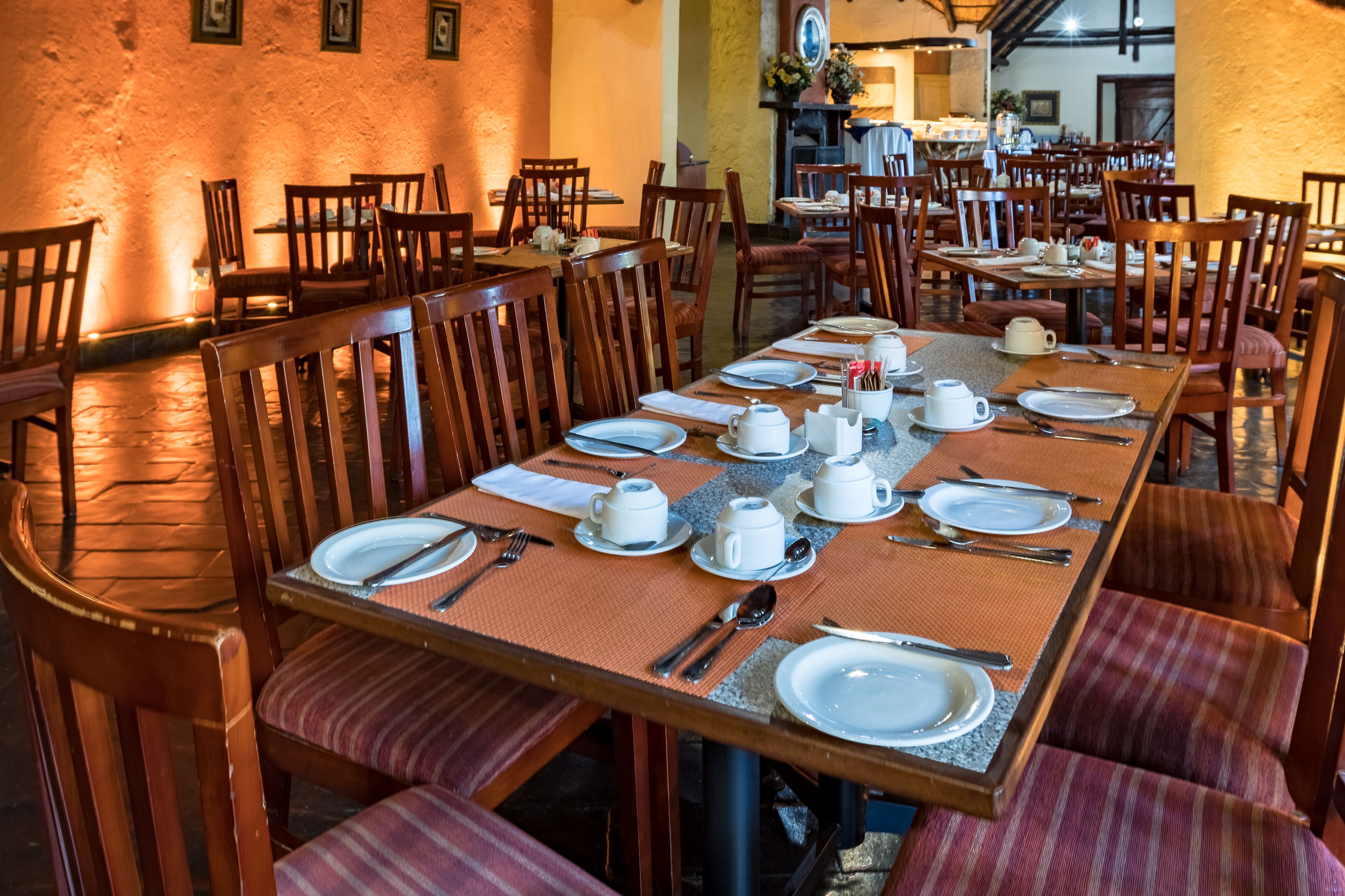 A dining area with multiple tables set for meals, wooden chairs, and a stone floor.
