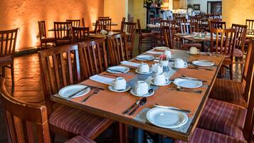 A dining area with multiple tables set for meals, wooden chairs, and a stone floor.