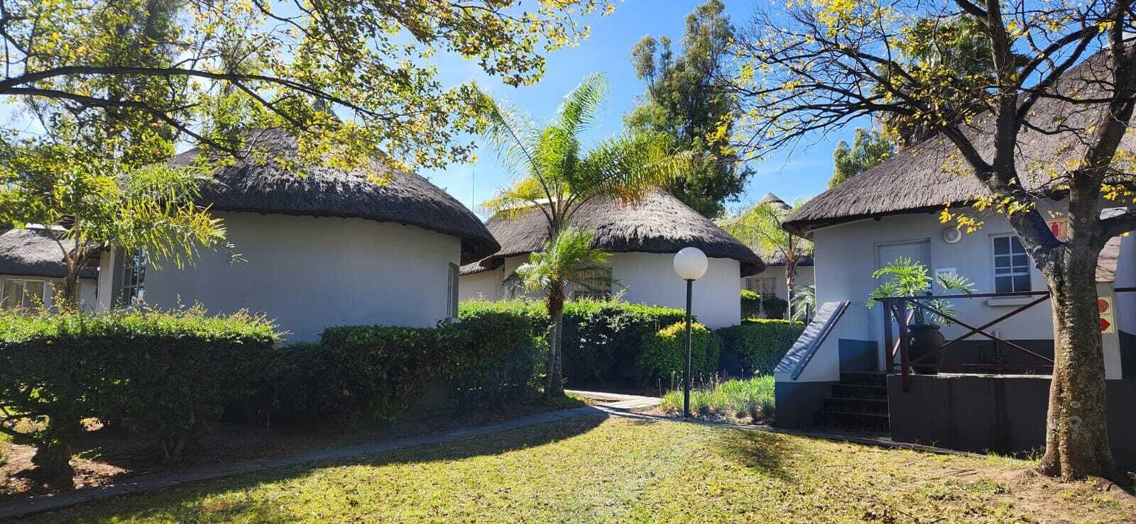 A courtyard with thatched-roof huts, surrounded by greenery and a clear sky.