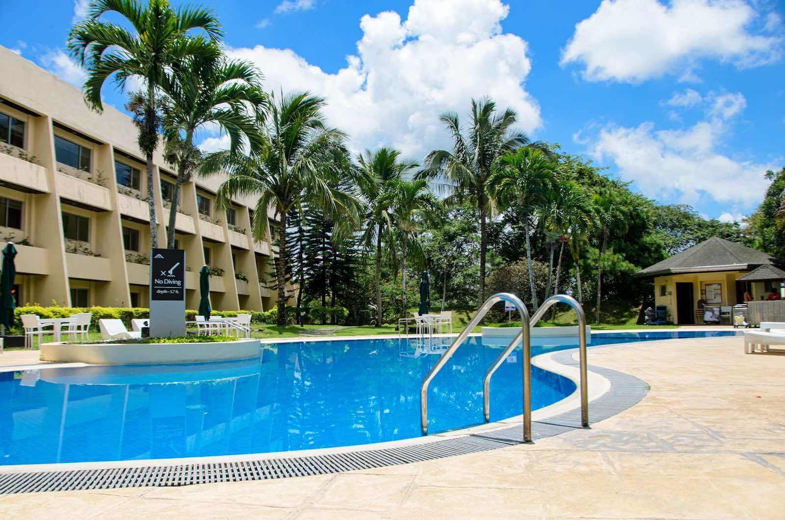 A swimming pool with no diving sign, surrounded by palm trees and a hotel building.