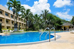 A swimming pool with no diving sign, surrounded by palm trees and a hotel building.