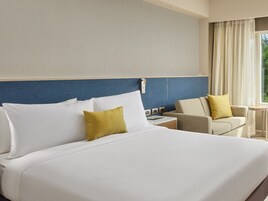 A hotel room with a large bed, a small desk, a chair, and a window with curtains.