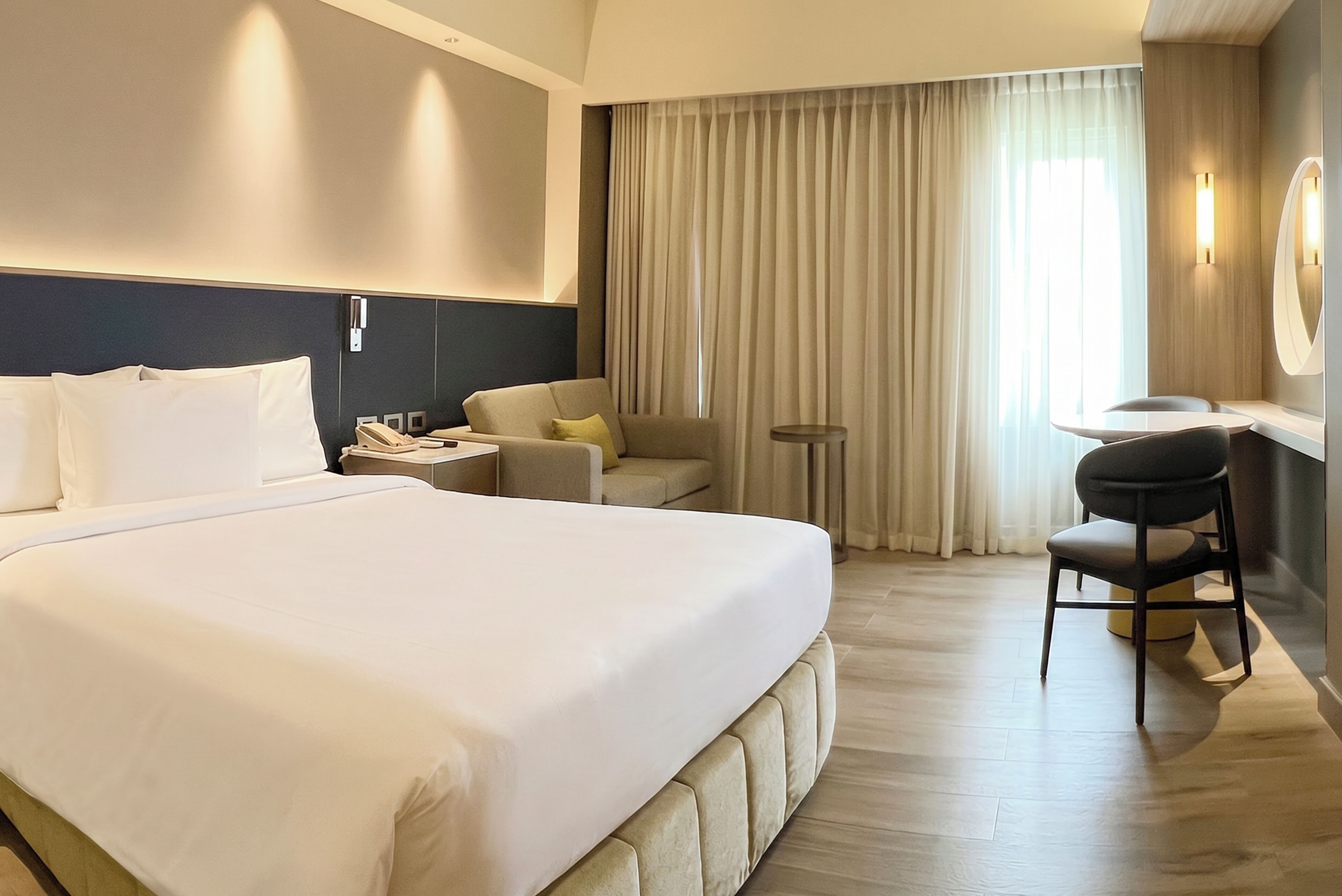 A hotel room with a large bed, a desk, a chair, a mirror, and a window with curtains.