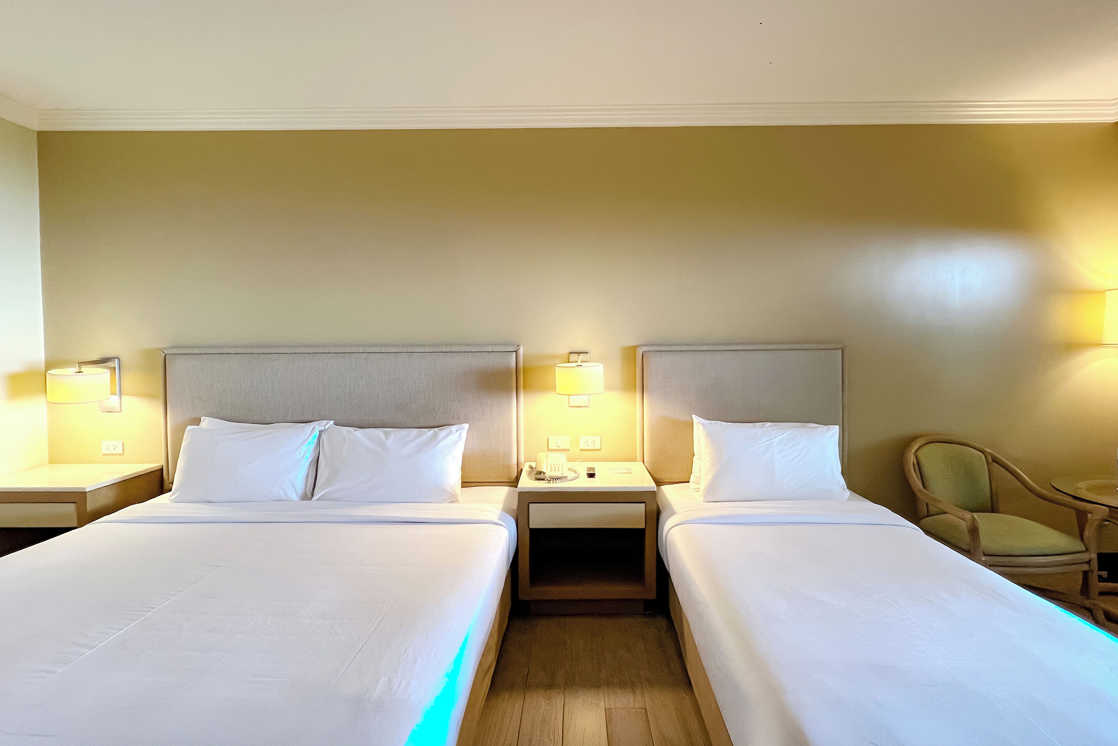 Habitación de hotel con dos camas, mesitas de noche, lámparas y una silla.