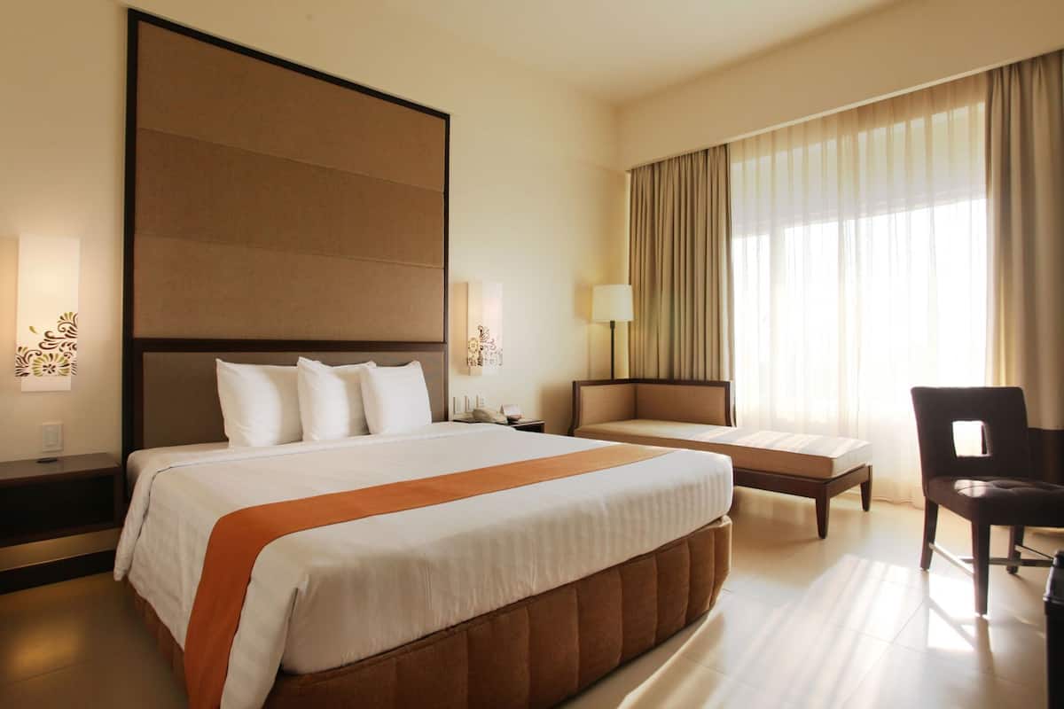 A hotel room with a large bed, a sofa, a chair, and a desk with a lamp.