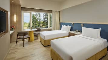 A hotel room with two beds, a dining table, a TV, and a window with a view of trees.