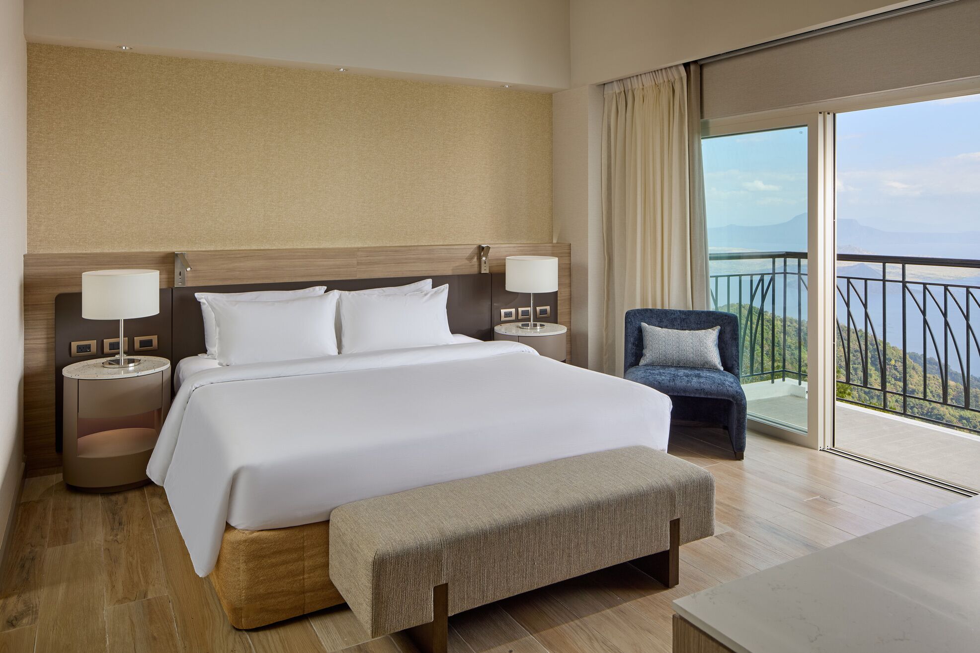 Camera d'albergo con un letto grande, due comodini con lampade, una panca e un balcone con vista.