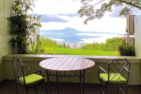 Un balcón con una mesa y sillas, vista a un paisaje montañoso y una masa de agua.