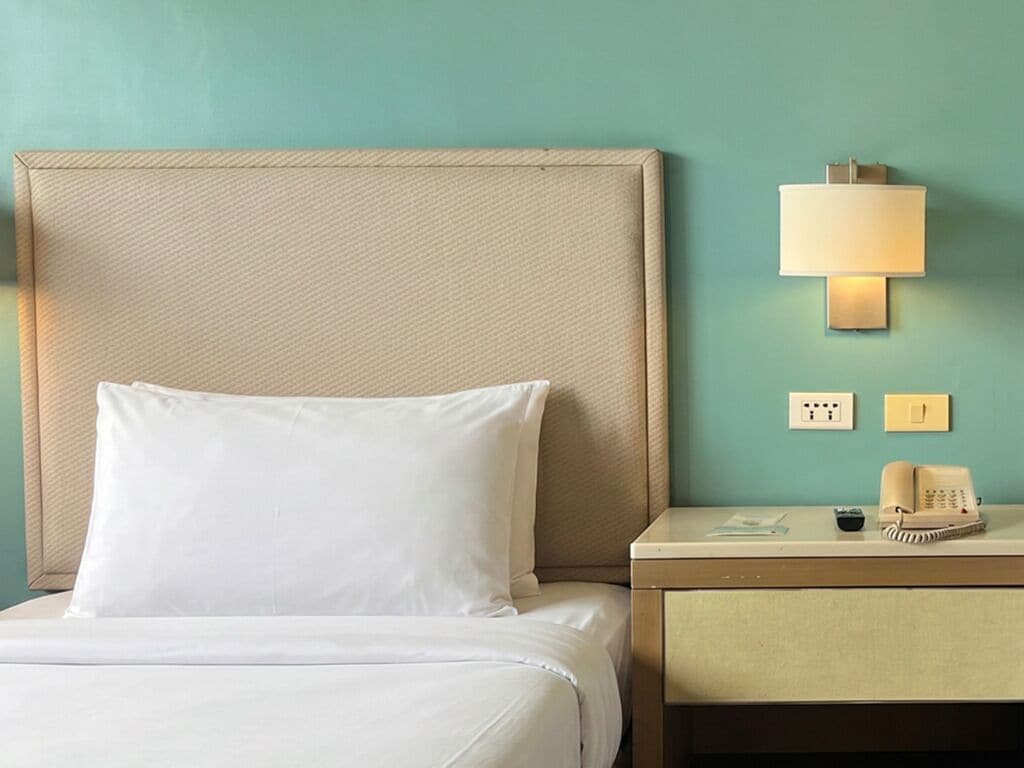 A hotel room with a bed, a nightstand, a lamp, a telephone, and a wall socket.