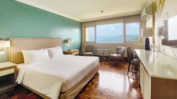 Habitación de hotel con cama, escritorio, dos sillas, ventana con vistas y una mesita.