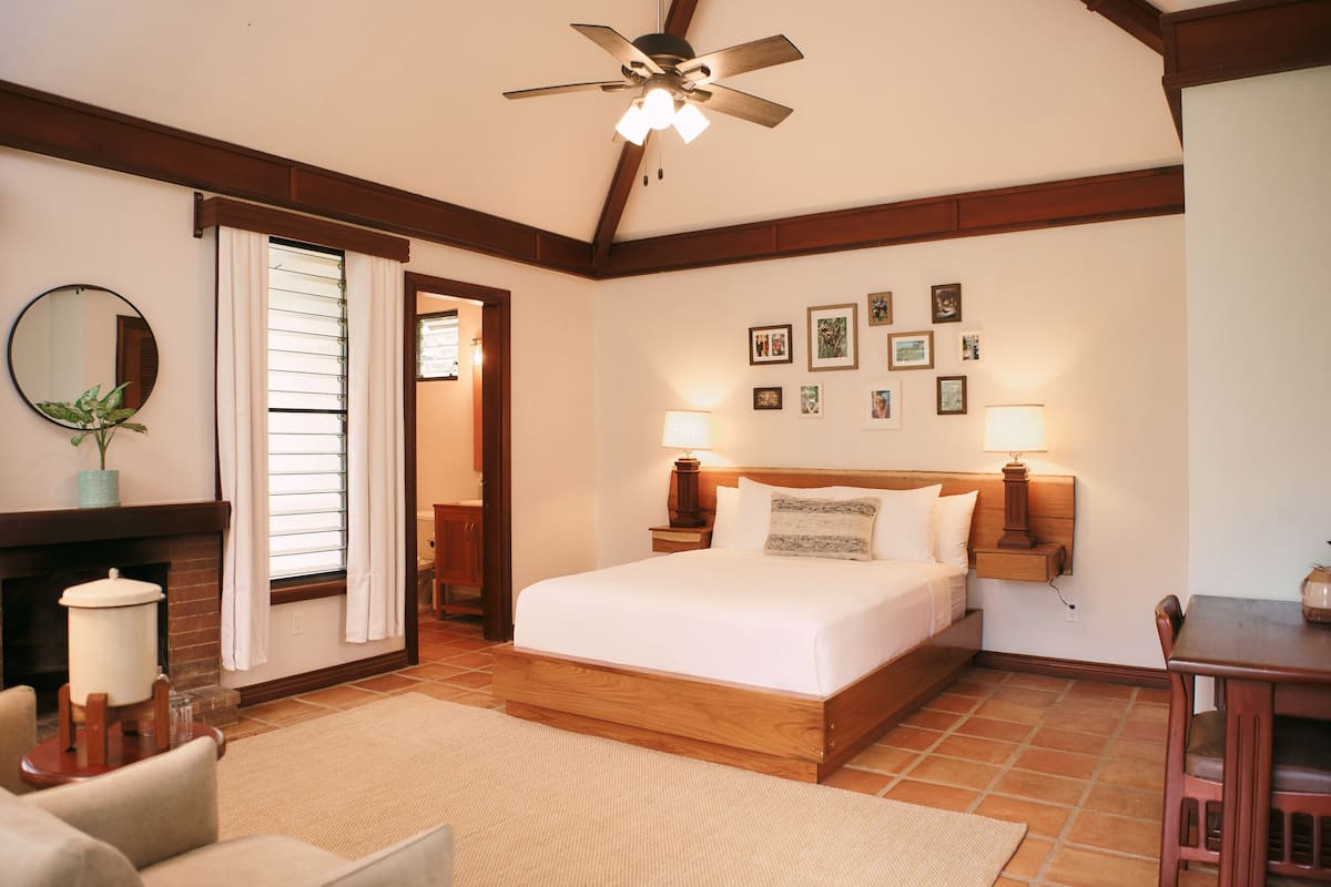 Un dormitorio con cama de madera, ventilador de techo, chimenea y zona de comedor.