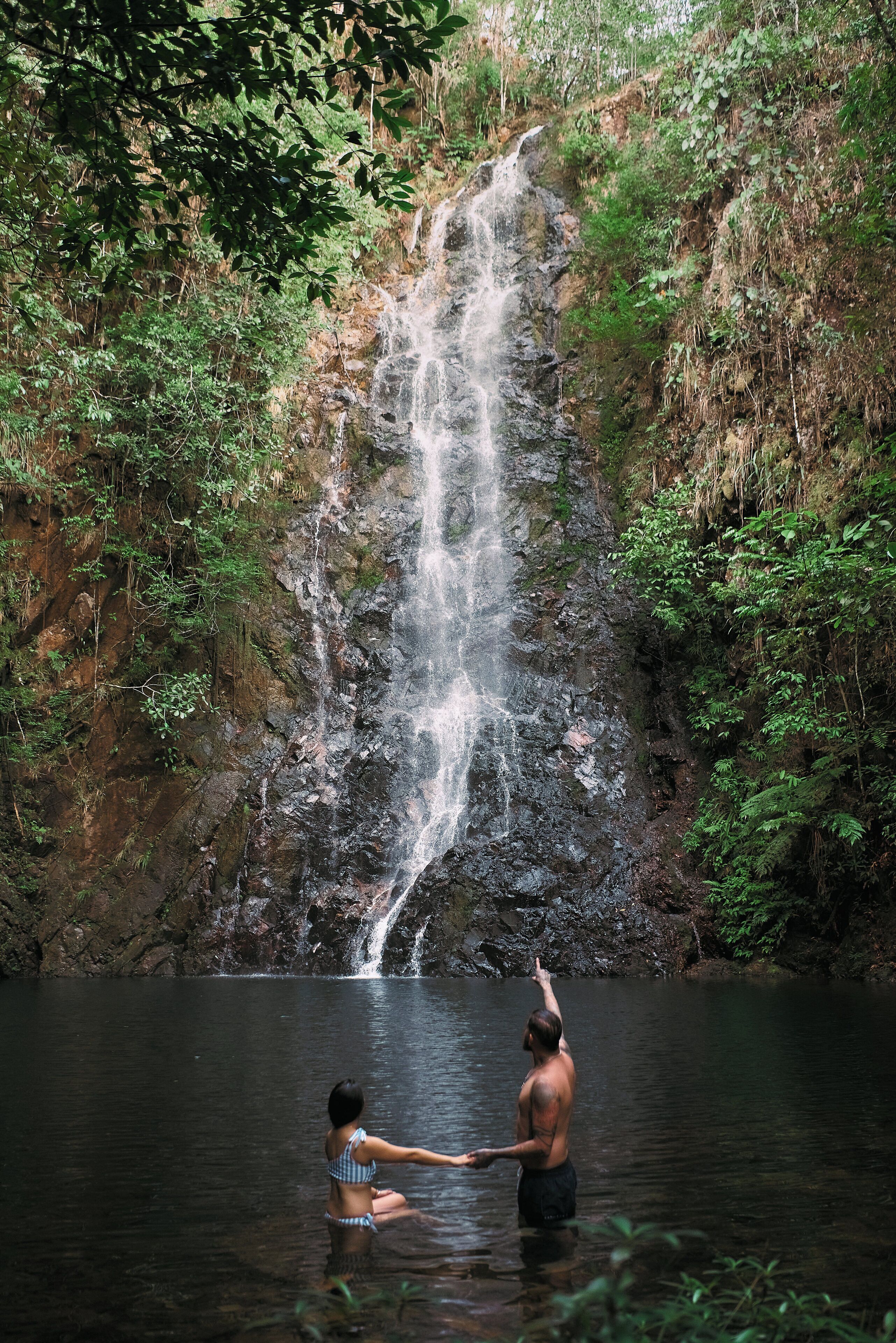 A waterfall in a forested area with two people in the water.