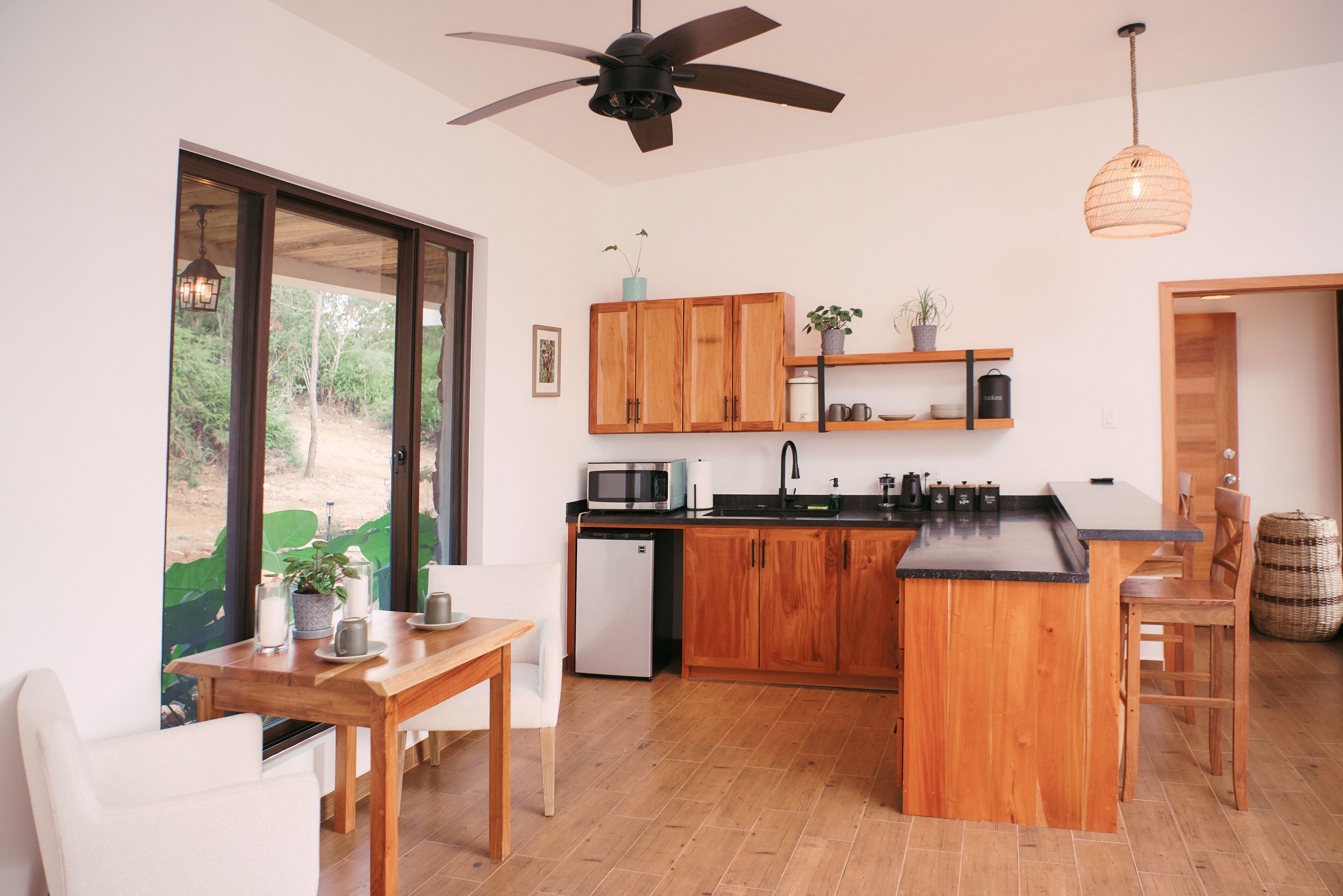 Una cocina moderna con armarios de madera, una isla central, un comedor con mesa y sillas, y vistas amplias a través de grandes ventanales.