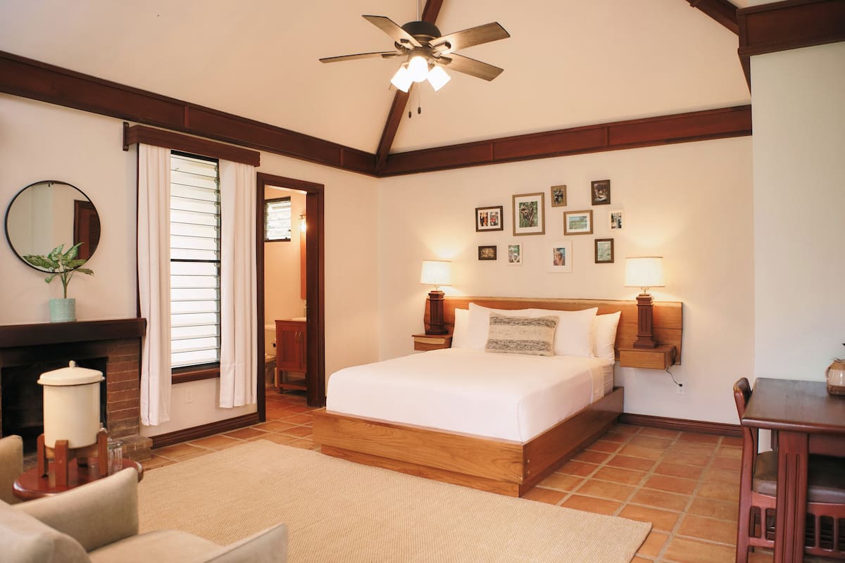 Un dormitorio con cama de madera, ventilador de techo, chimenea y zona de comedor.