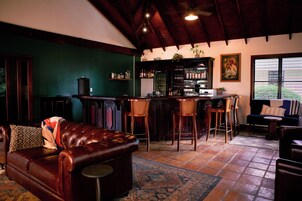 Un rincón acogedor con bar de madera, dos taburetes altos y una zona de estar con sofá y sillones de cuero.