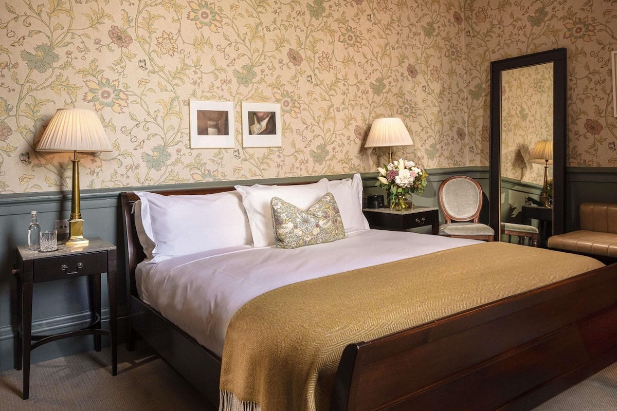 Une chambre à coucher bien aménagée, avec un grand lit, deux tables de chevet, un miroir et un papier peint à motifs floraux.