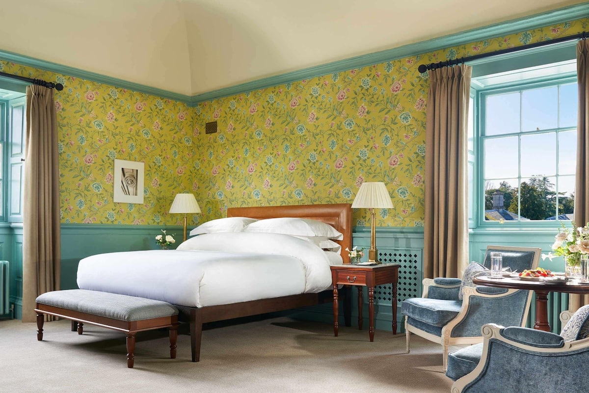 Une chambre bien aménagée, dotée d’un grand lit, de deux tables de chevet avec des lampes, d’une petite table ornée d’un vase de fleurs et d’un fauteuil.
