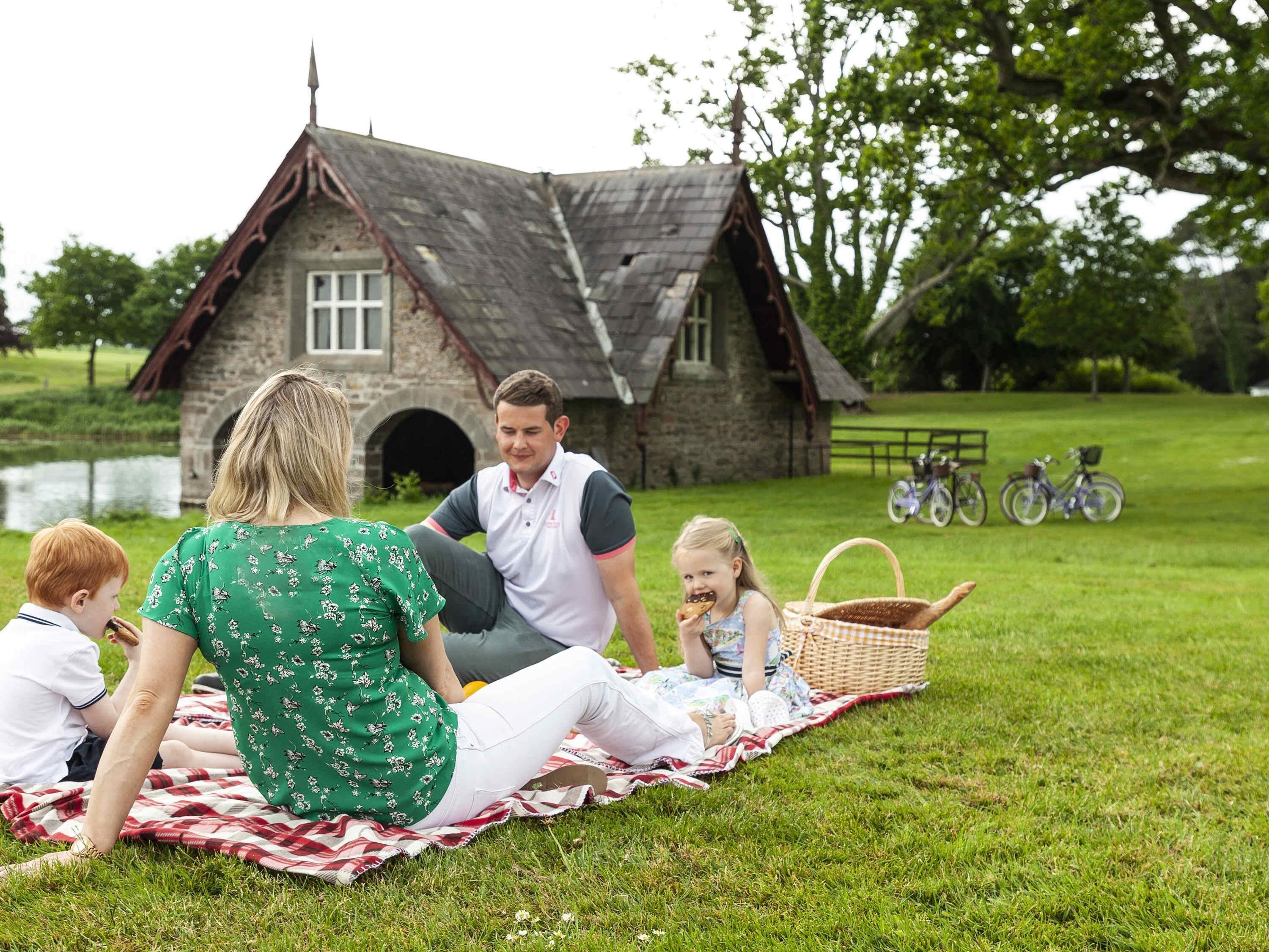 Un pique-nique en famille dans un champ verdoyant, avec un bâtiment en pierre en arrière-plan.