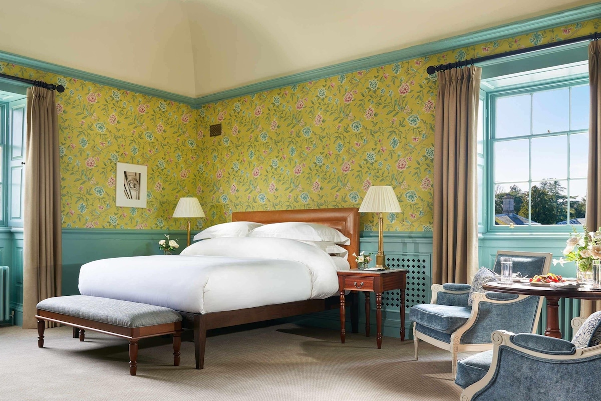 A well-appointed bedroom with a large bed, two bedside tables with lamps, a small table with a vase of flowers, and a chair.