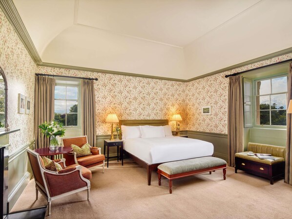 A hotel room with a bed, two bedside tables, a chair, a bench, and a window with curtains.