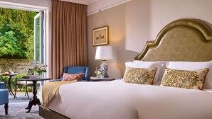 A hotel room with a large bed, two armchairs, a small table, and a view of greenery through a window.