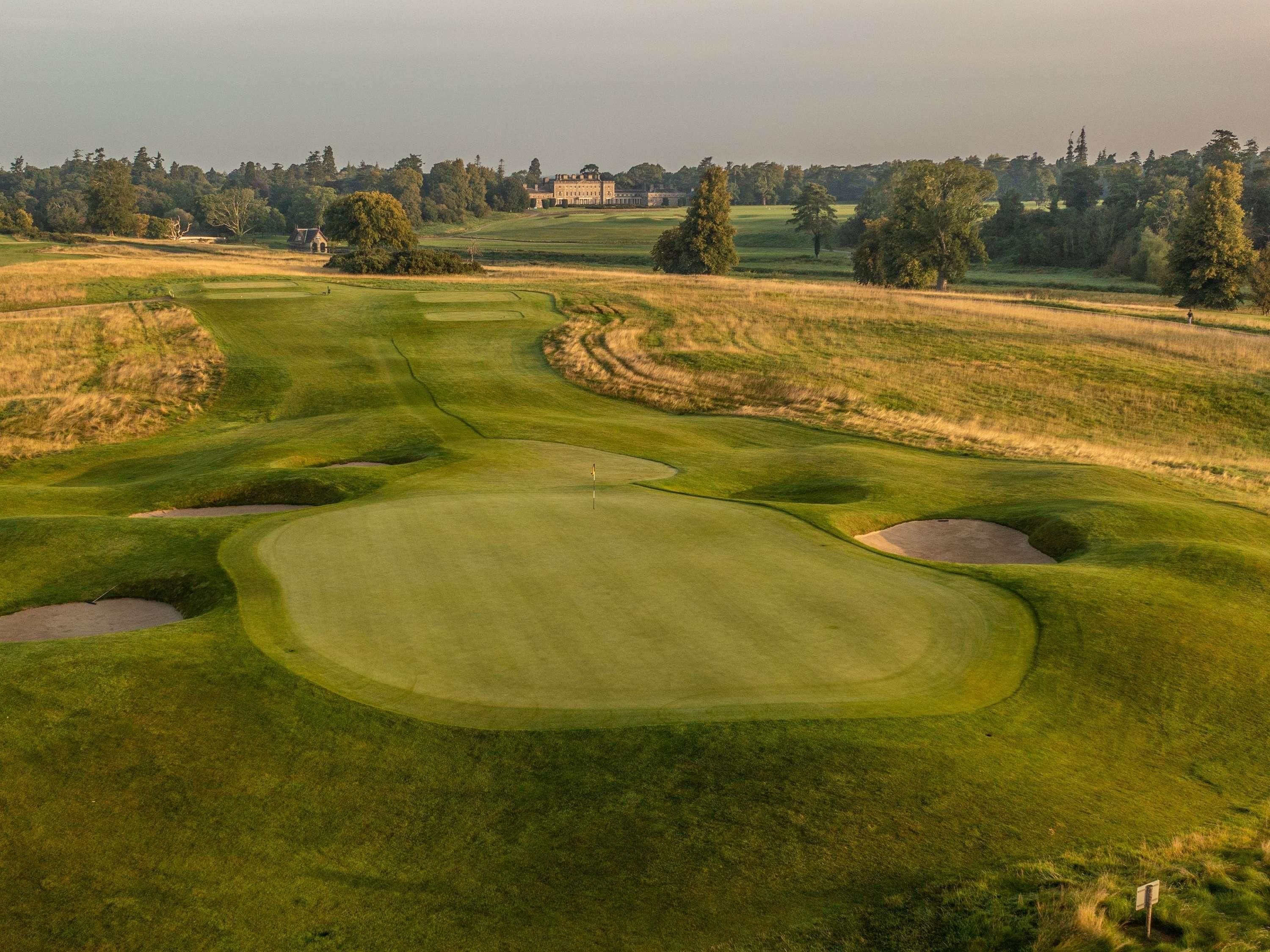 A golf course with bunkers, a putting green, and a distant building.