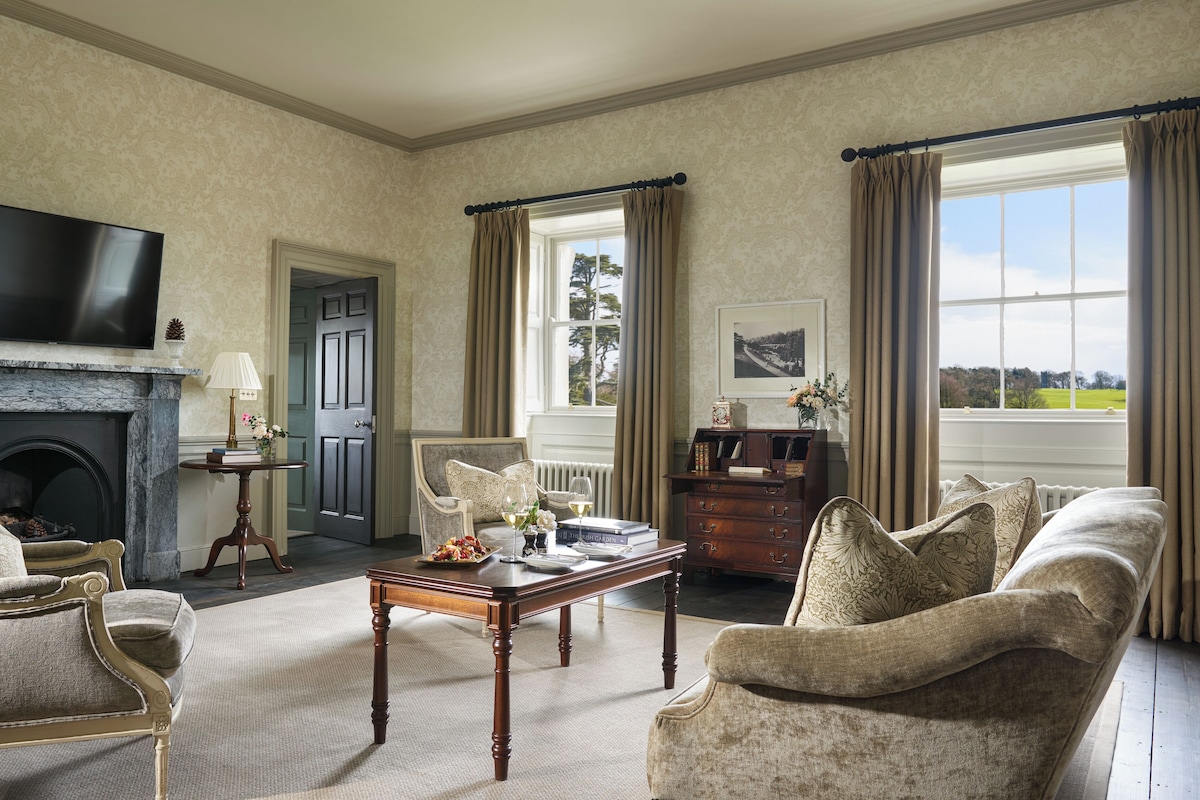 A spacious living room with a fireplace, comfortable seating, a television, and a view of the outdoors.