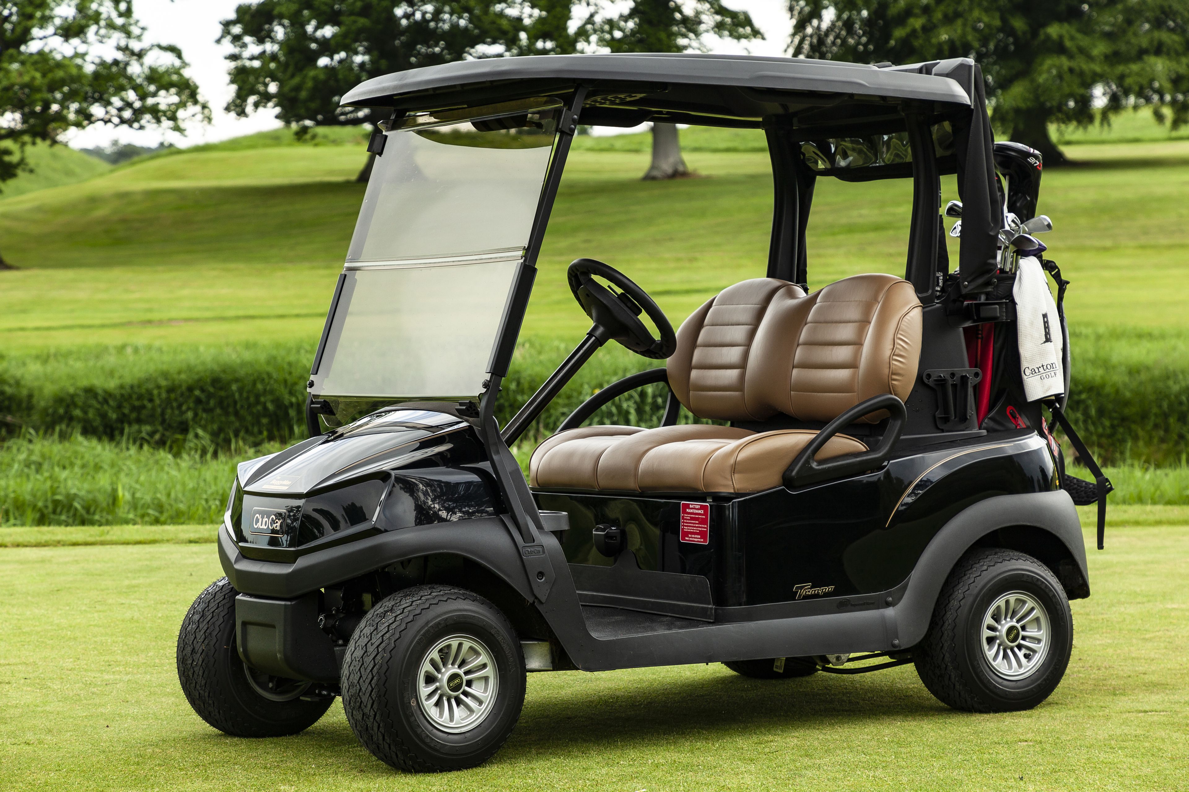 Un carrito de golf con carrocería negra y asientos de cuero color beige, estacionado sobre un campo cubierto de césped.