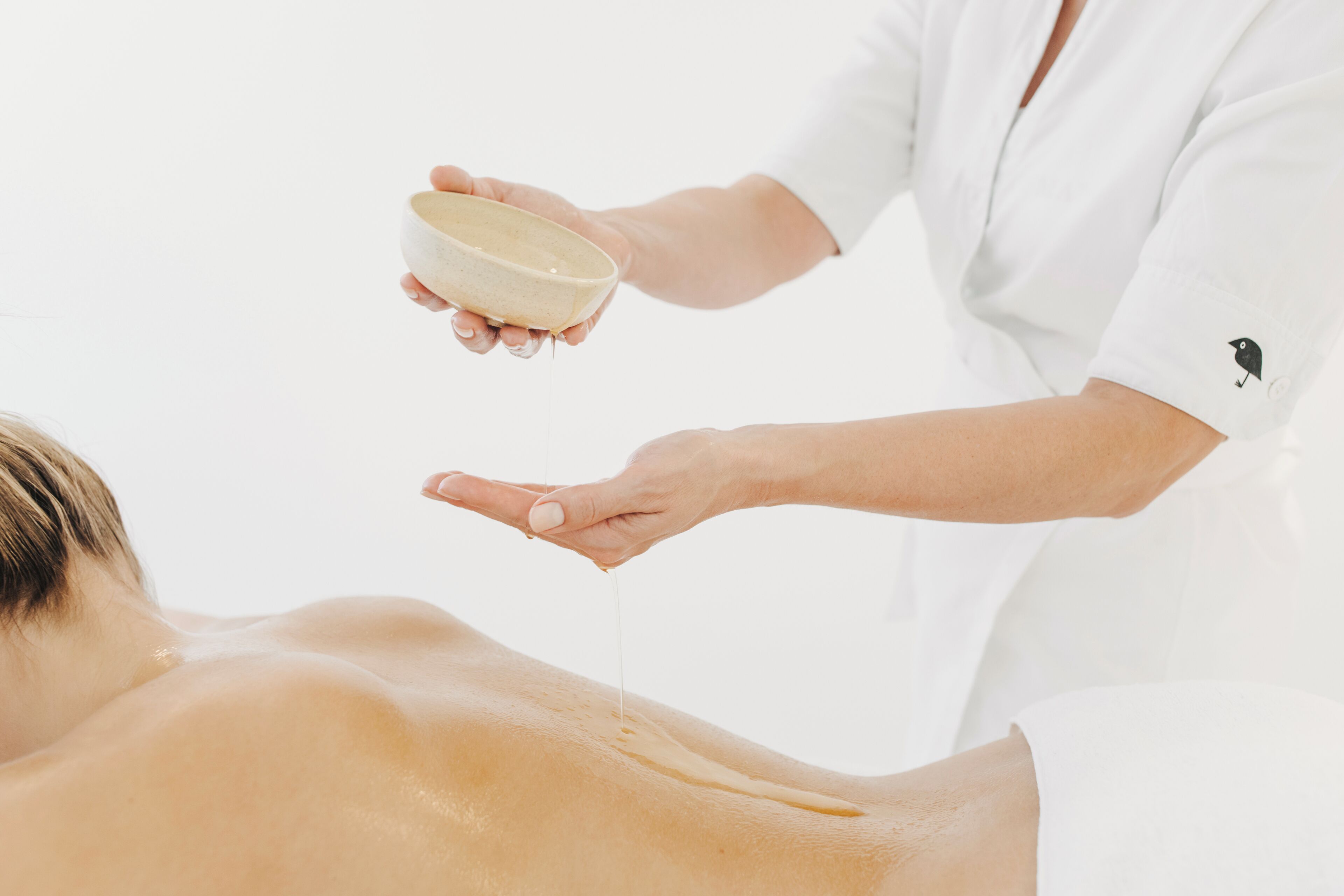 A person receiving a massage with a bowl of oil being poured onto their back.
