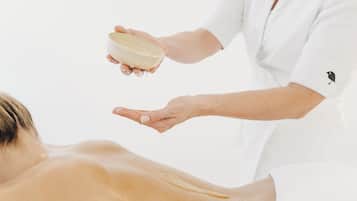 A person receiving a massage with a bowl of oil being poured onto their back.