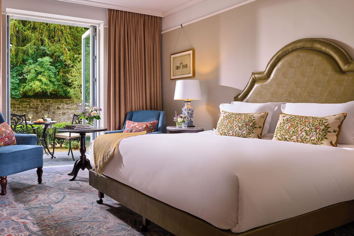 Une chambre d’hôtel avec un grand lit, deux chaises, une table et une vue sur la verdure.