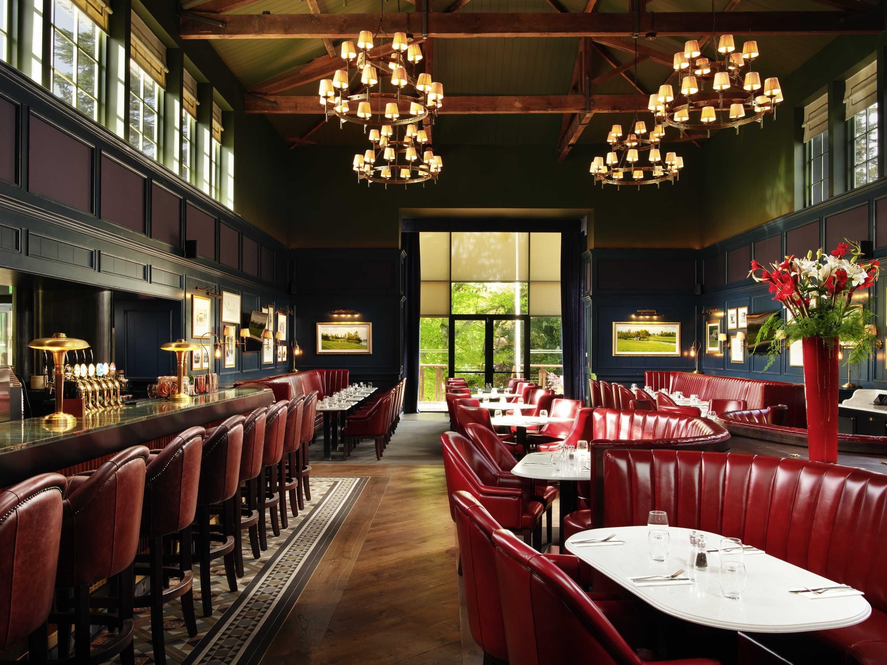 A restaurant interior with high ceilings, chandeliers, leather booths, and a bar area.