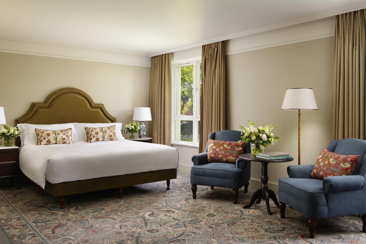 A hotel room with a large bed, two armchairs, a small table, and a floor lamp.