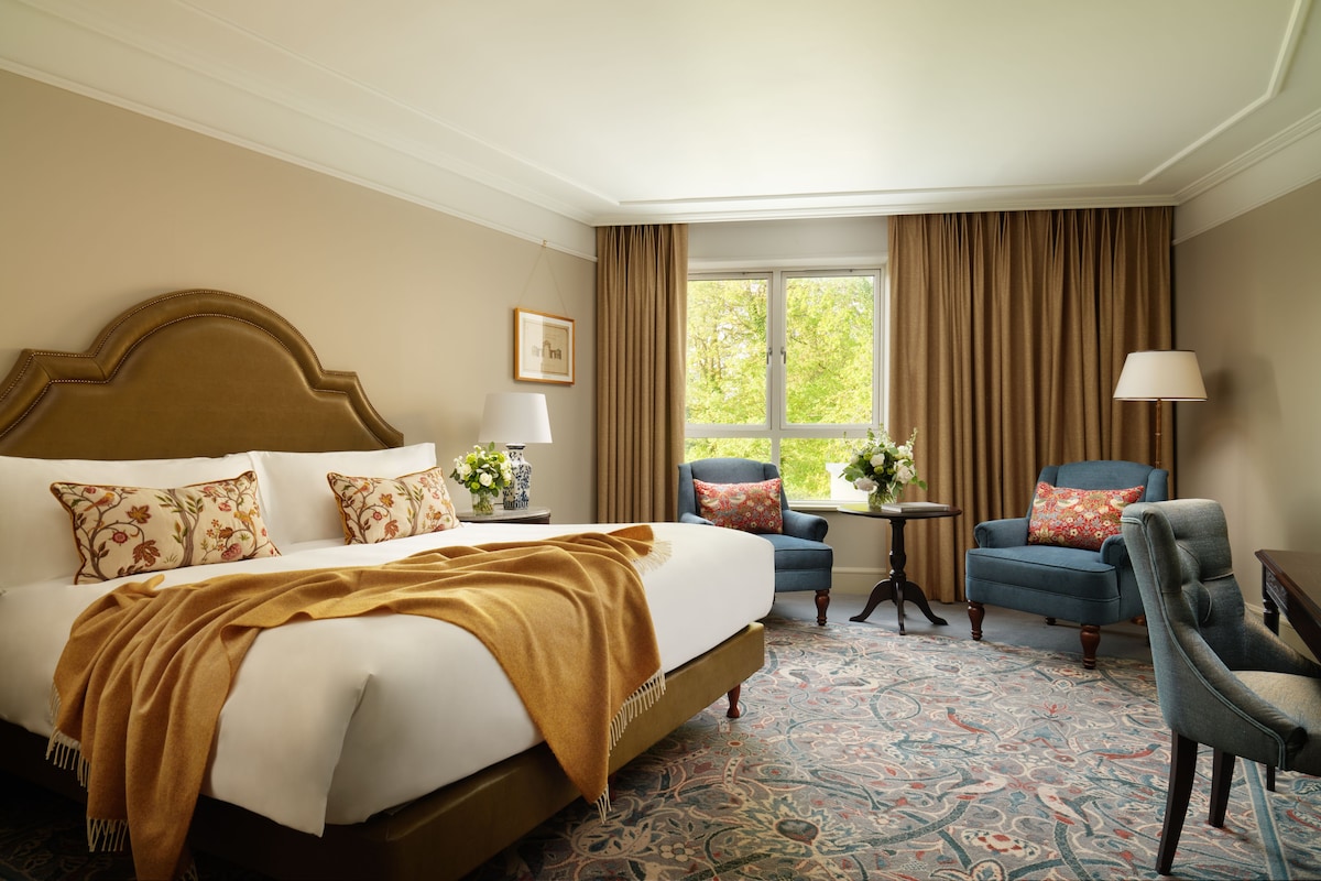 A hotel room with a large bed, two armchairs, a small table, and a window with curtains.
