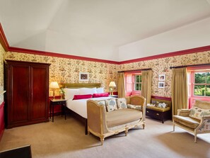 A bedroom with a bed, two chairs, a wardrobe, and a window with curtains.