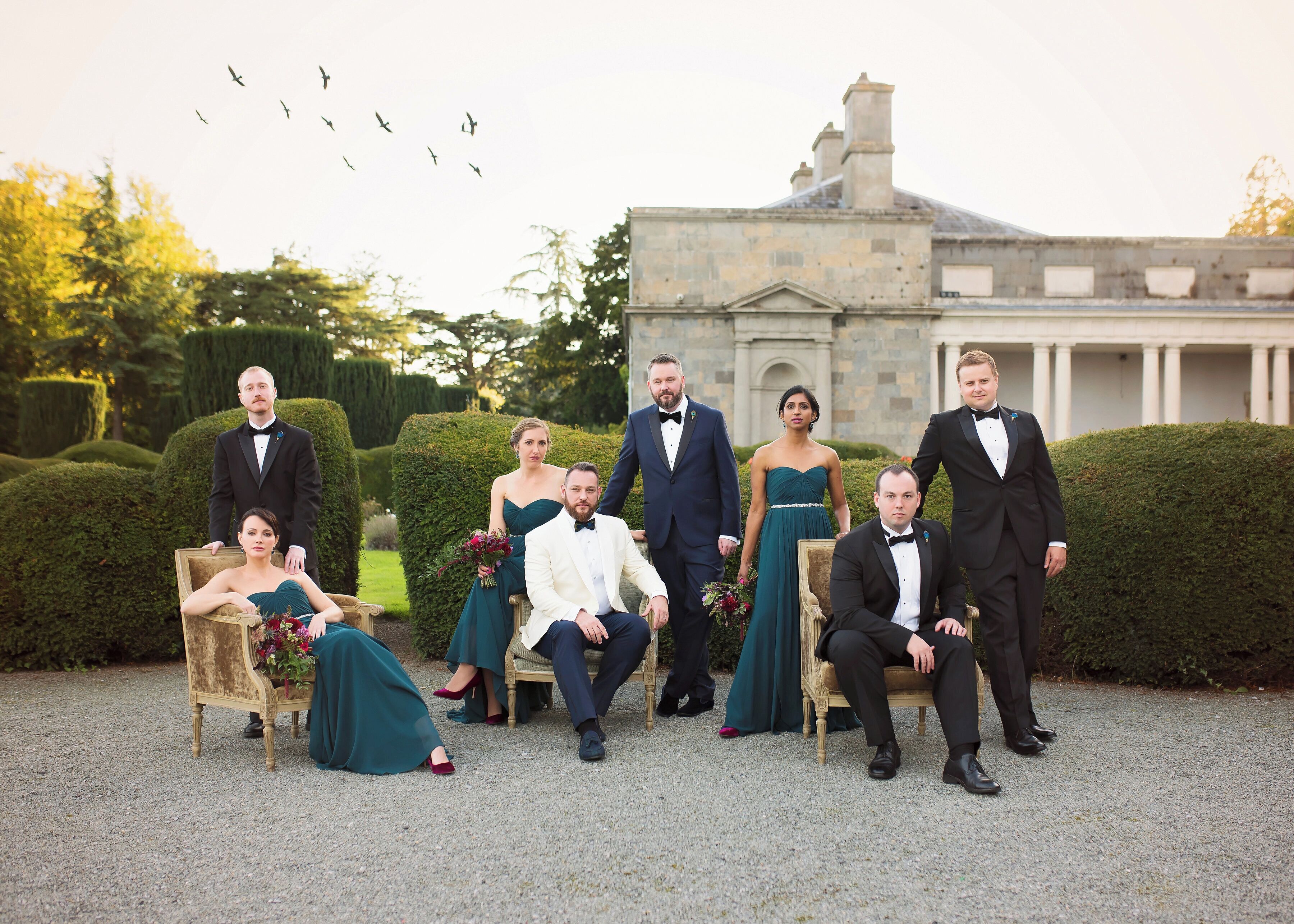 A group of people in formal attire seated and standing in front of a building with a classical architectural style.