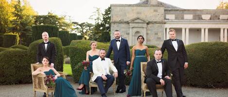 A group of people in formal attire seated and standing in front of a building with a classical architectural style.