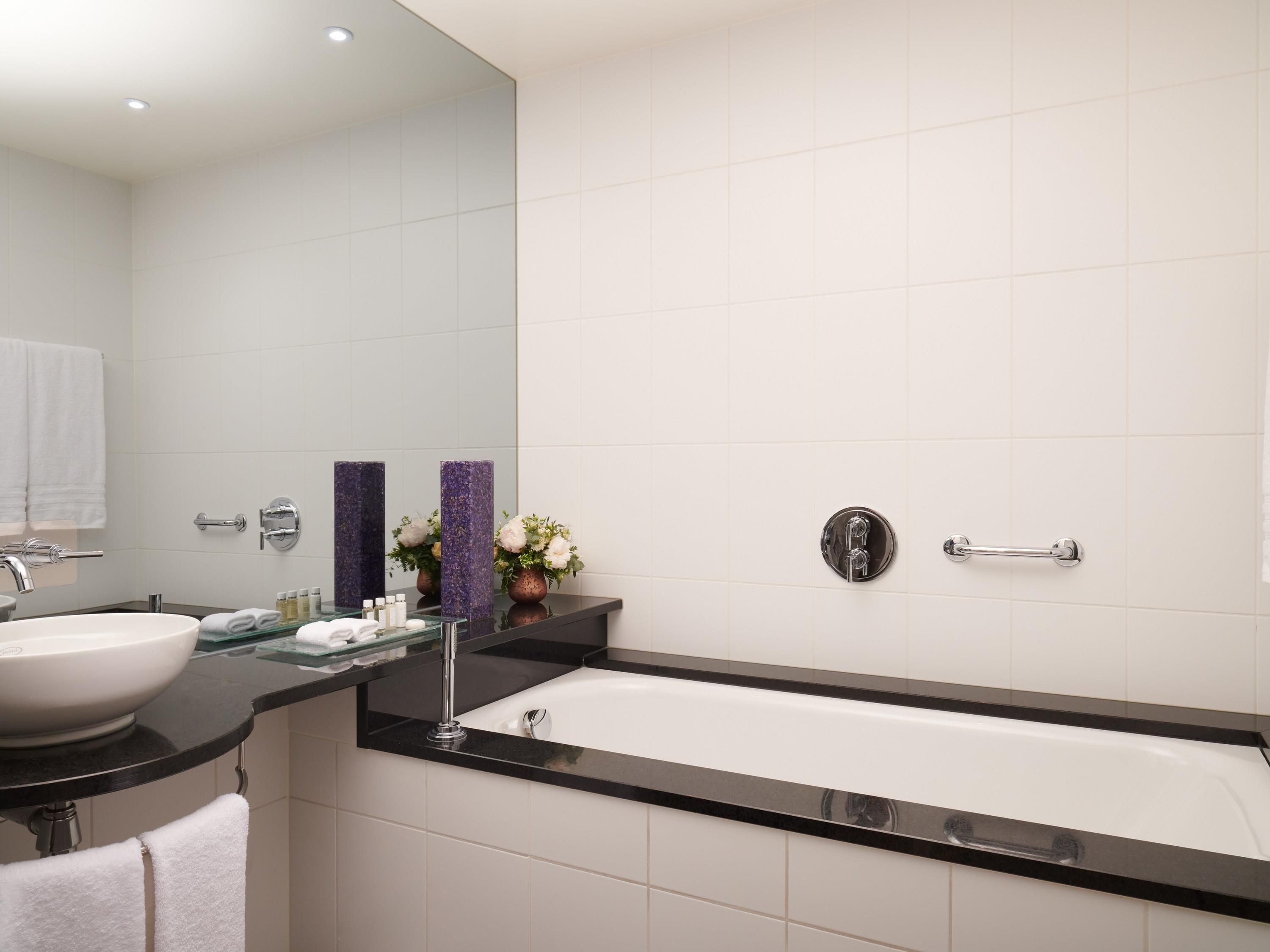 A modern bathroom with a white bathtub, a black countertop, a large mirror, and a white sink.