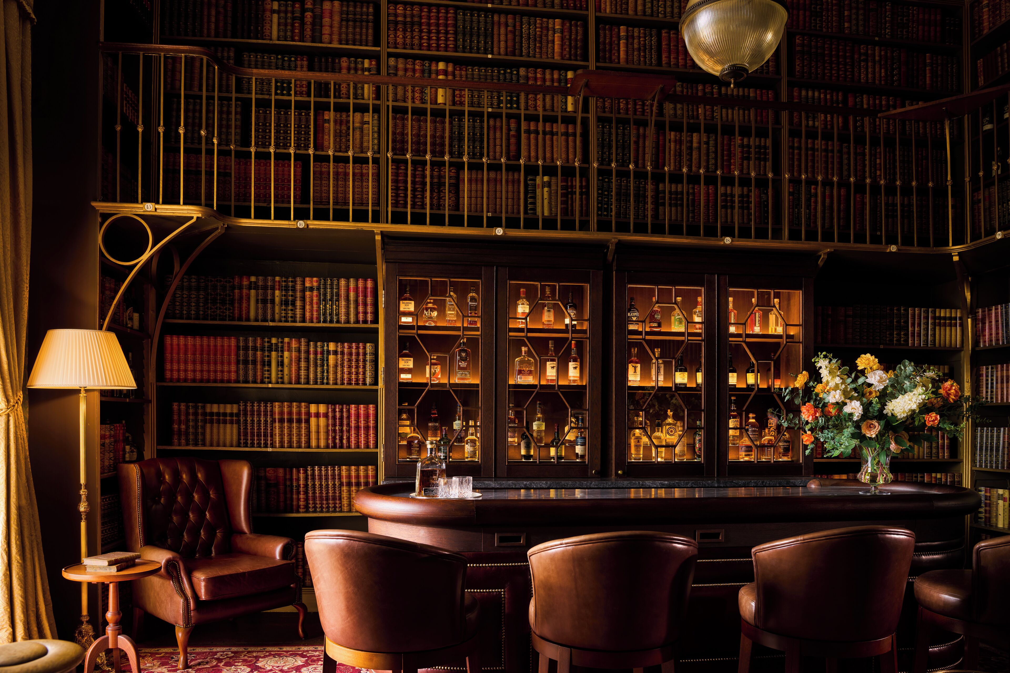A bar area with leather chairs, a bar counter, and a bookshelf filled with books.