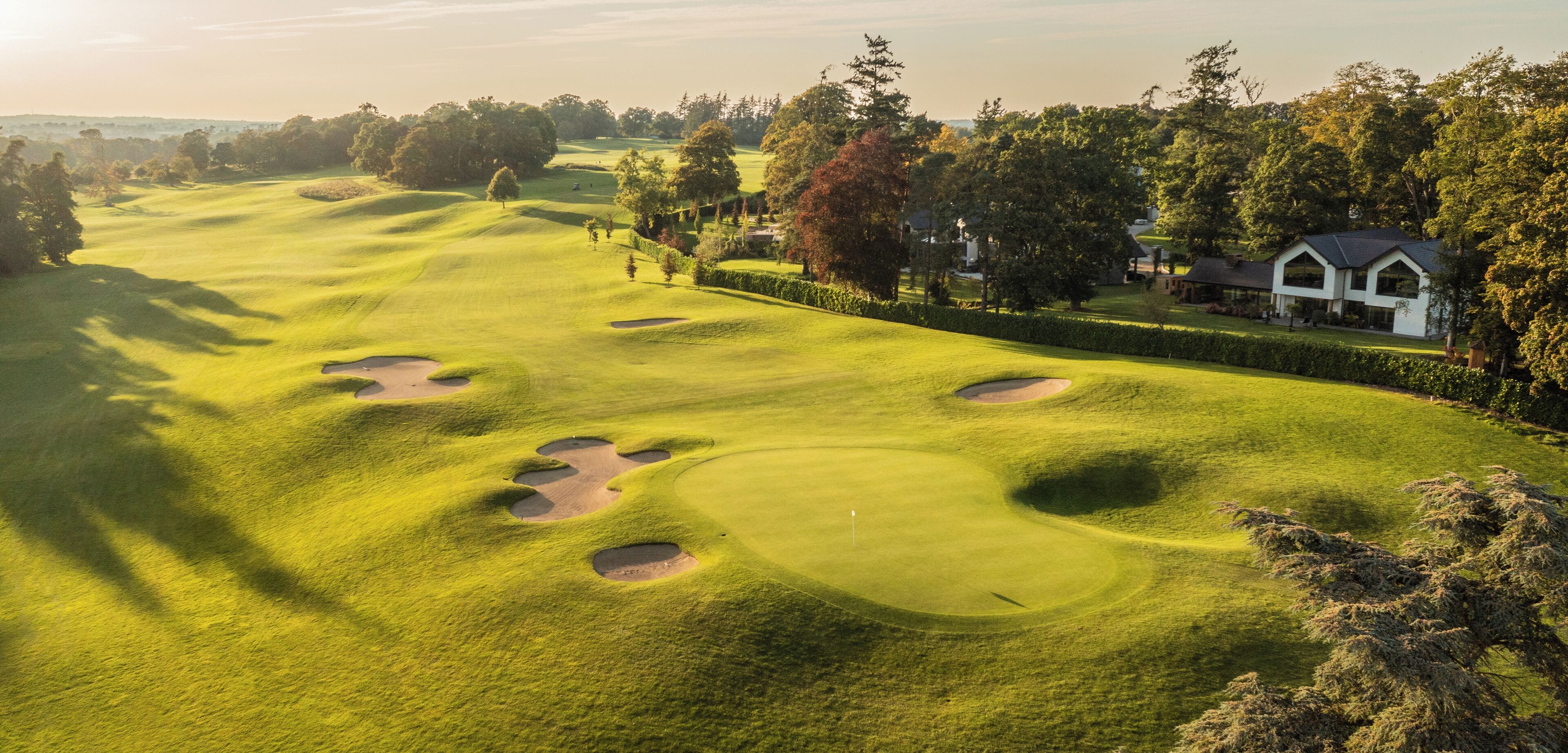 A golf course with bunkers, a clubhouse, and surrounding trees.