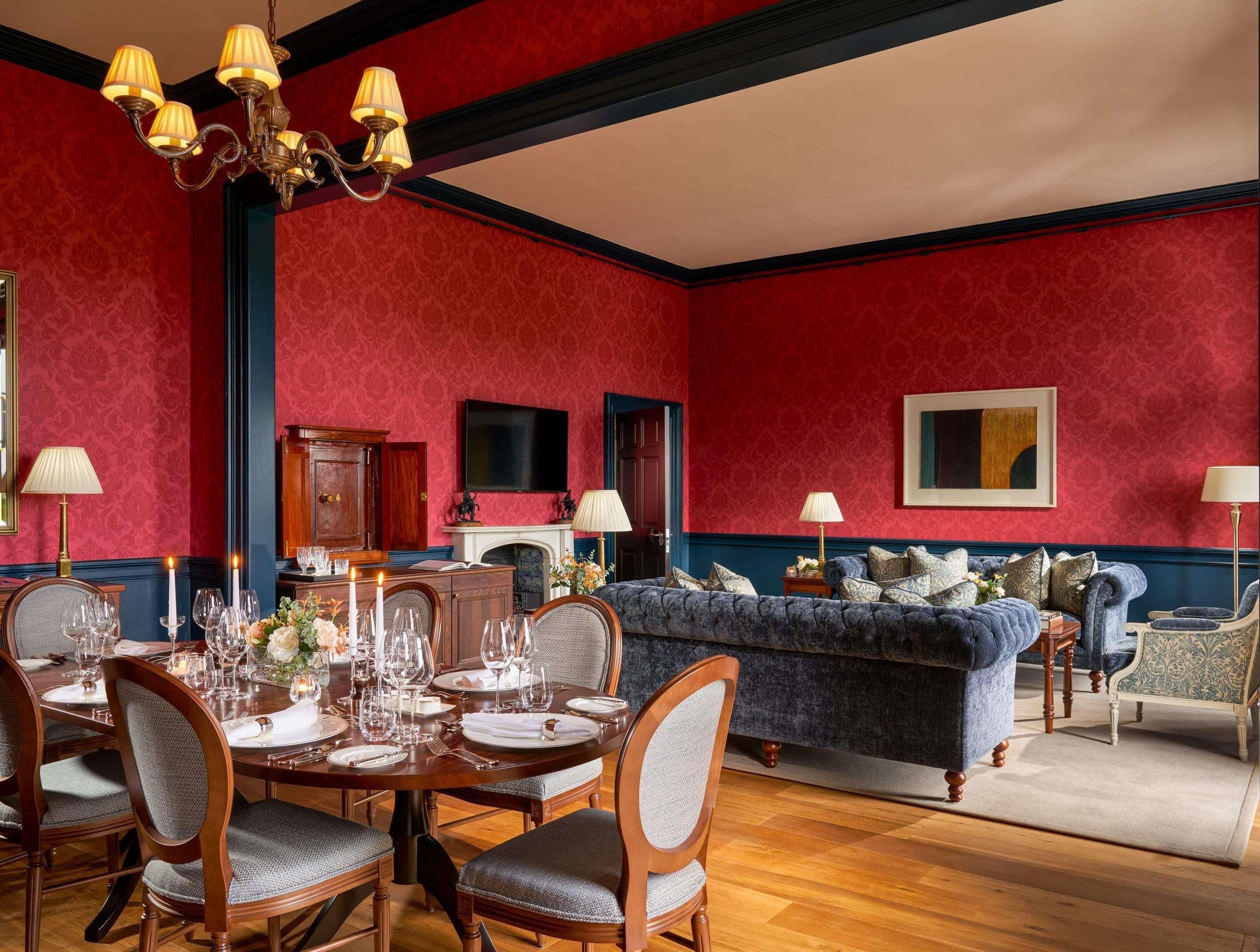 A dining room with a wooden table set for six, flanked by two chairs, and a blue sofa in the background.