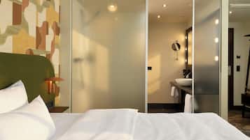 Habitación de hotel con cama, espejo en la pared, baño con lavamanos y pared con diseño.