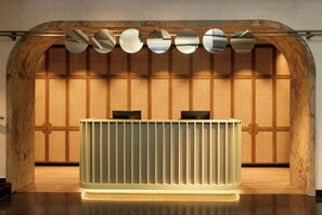 A reception desk with a modern design, situated in a lobby with a wooden wall and a tiled floor. - The Cloud One München-Hauptbahnhof (Munich)