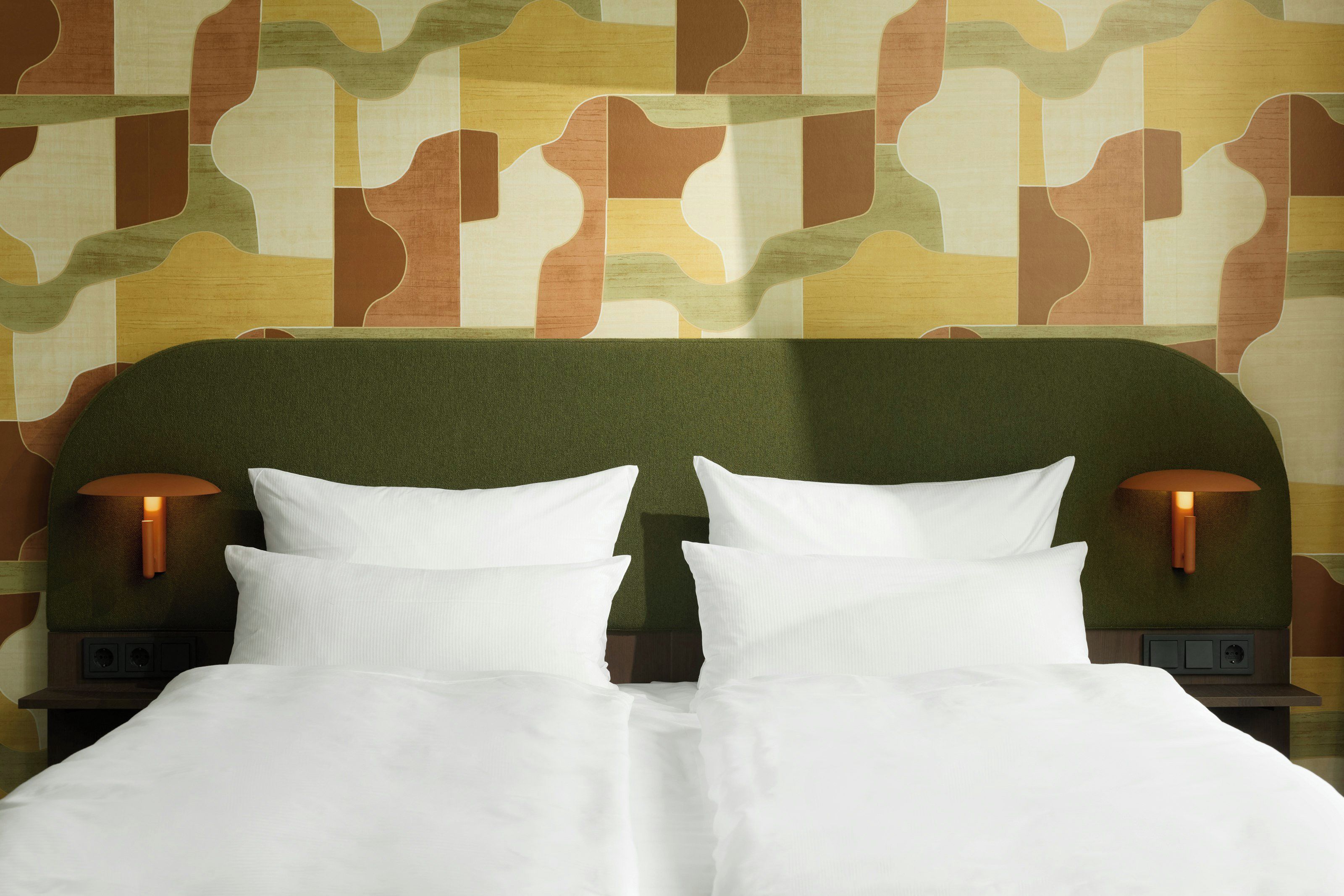 Een bed met witte beddengoed, twee wandlampen en een behang met patroon.