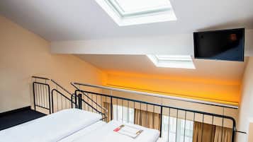 Ein Hotelzimmer mit einem Bett, einem an der Wand montierten Fernseher, einem Fenster mit Vorhängen und einer Treppe.